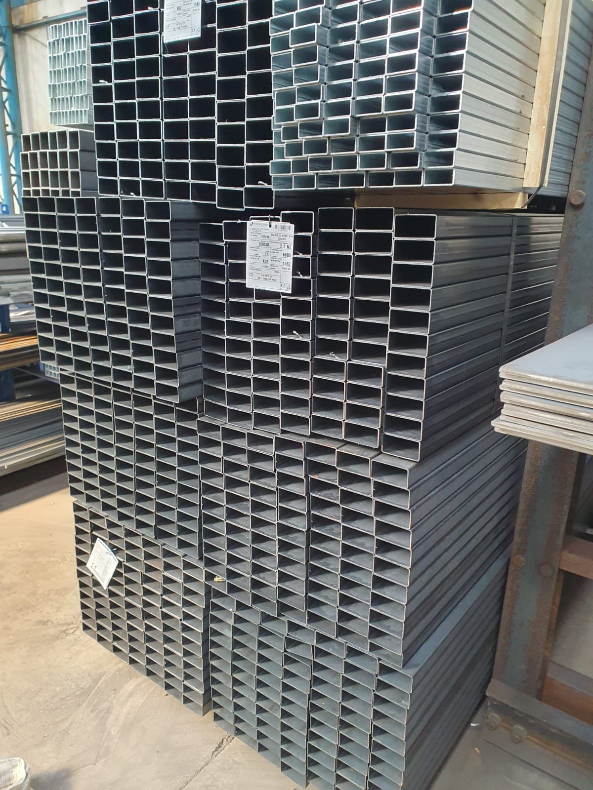 Pile di tubi rettangolari in acciaio, metallo grigio, in un magazzino.