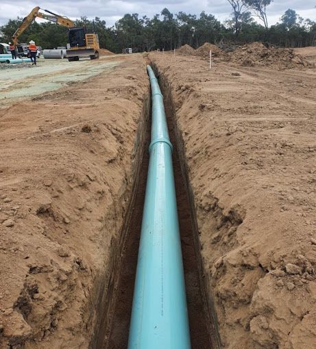 Freshly Excavated Drainage Tunnel  with a green pipe and yellow Excavator - Plumber in Mount Low, QLD