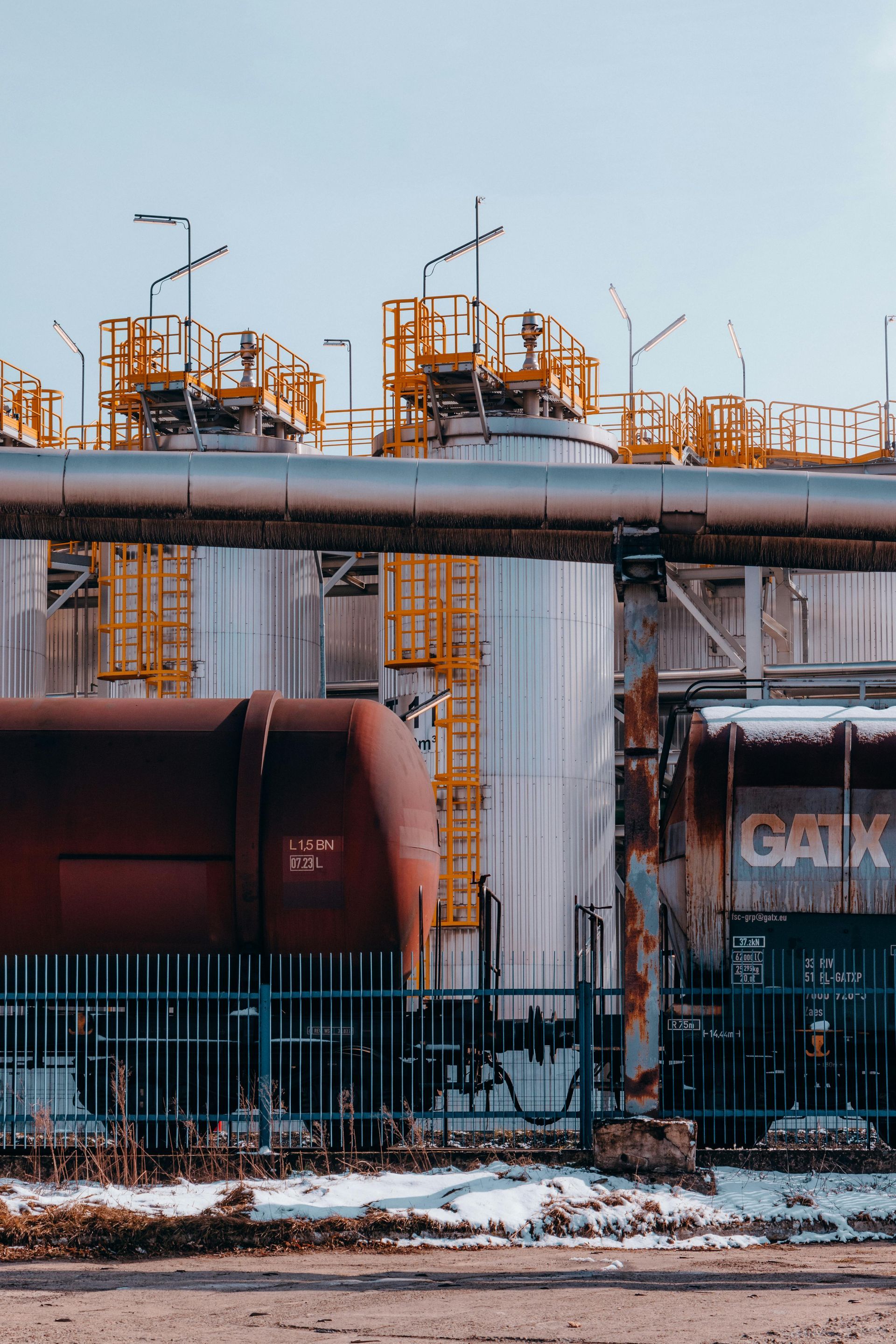 A train is parked under a bridge in front of a factory.