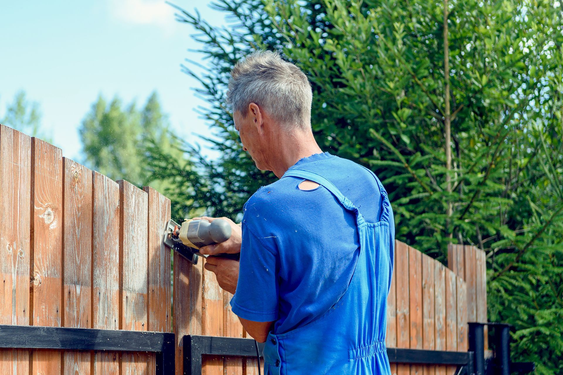 A man is fixing a wooden fence with a drill.