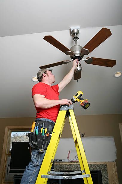 A man is standing on a ladder fixing a ceiling fan.