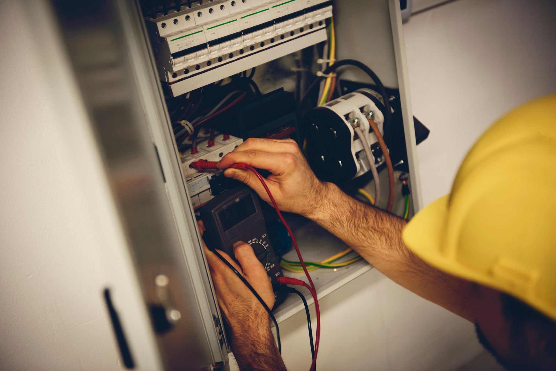 A man wearing a hard hat is working on an electrical box.