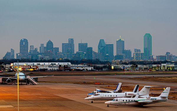 A couple of planes are parked on a runway with a city skyline in the background