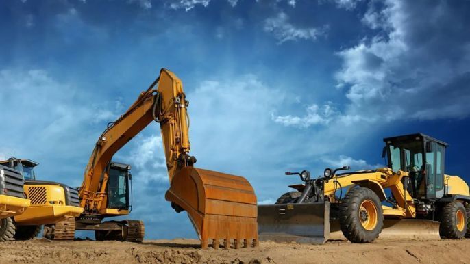 A bulldozer and an excavator are sitting on top of a dirt field.
