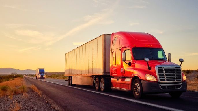 A red semi truck is driving down a highway at sunset.
