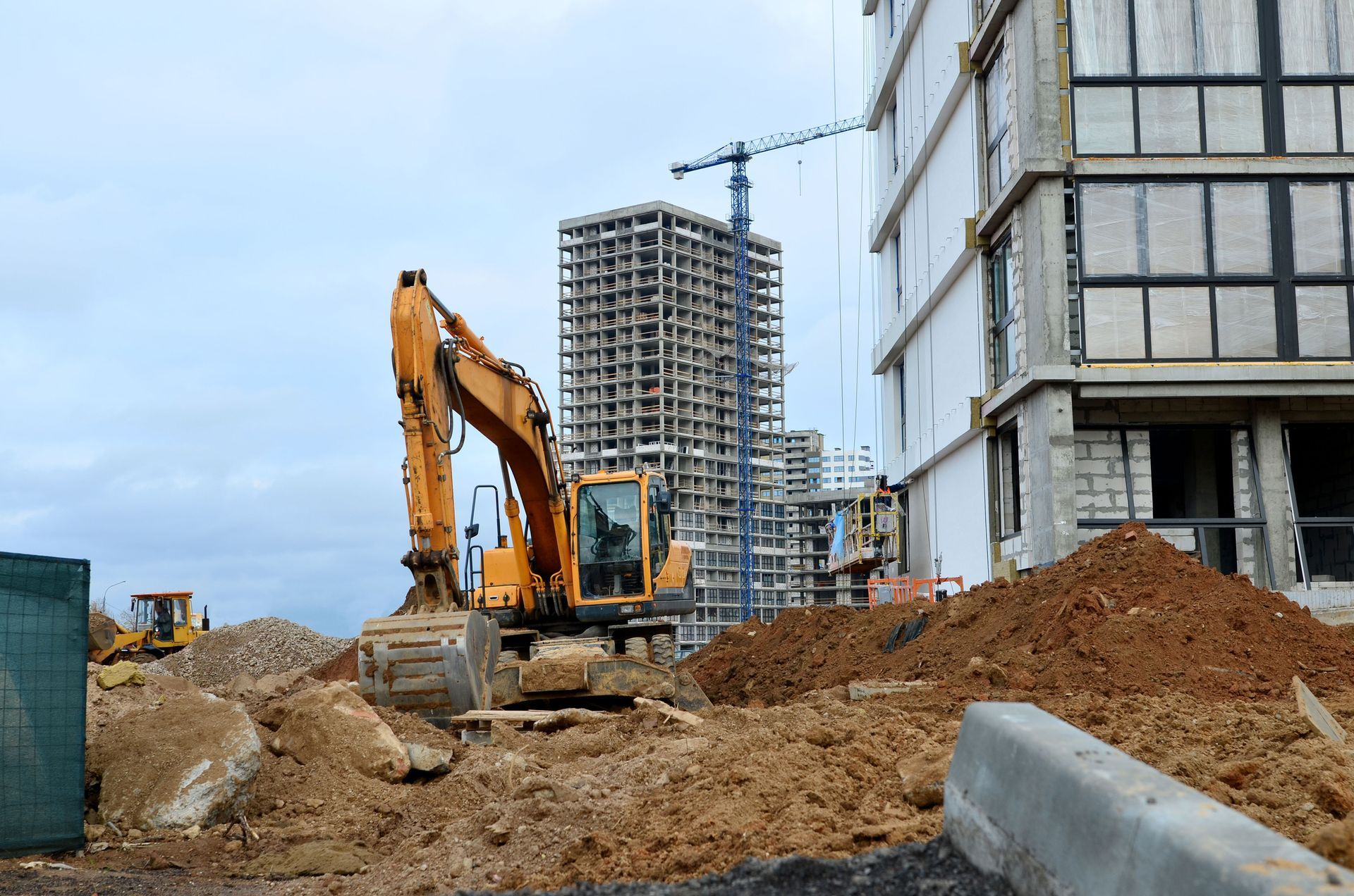 An excavator is working on a construction site in front of a building under construction.