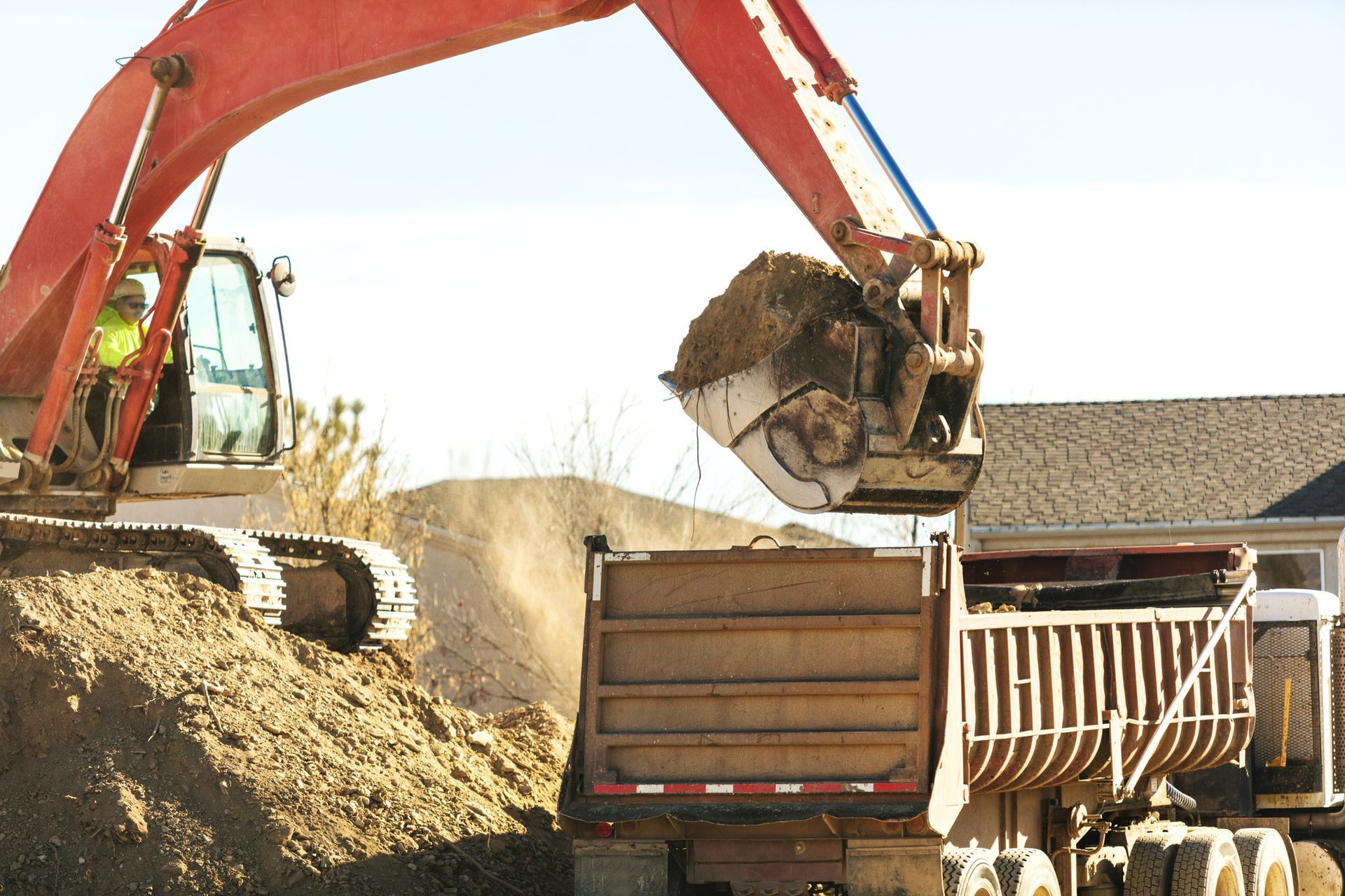 An red excavator is loading dirt into a rusty dump truck