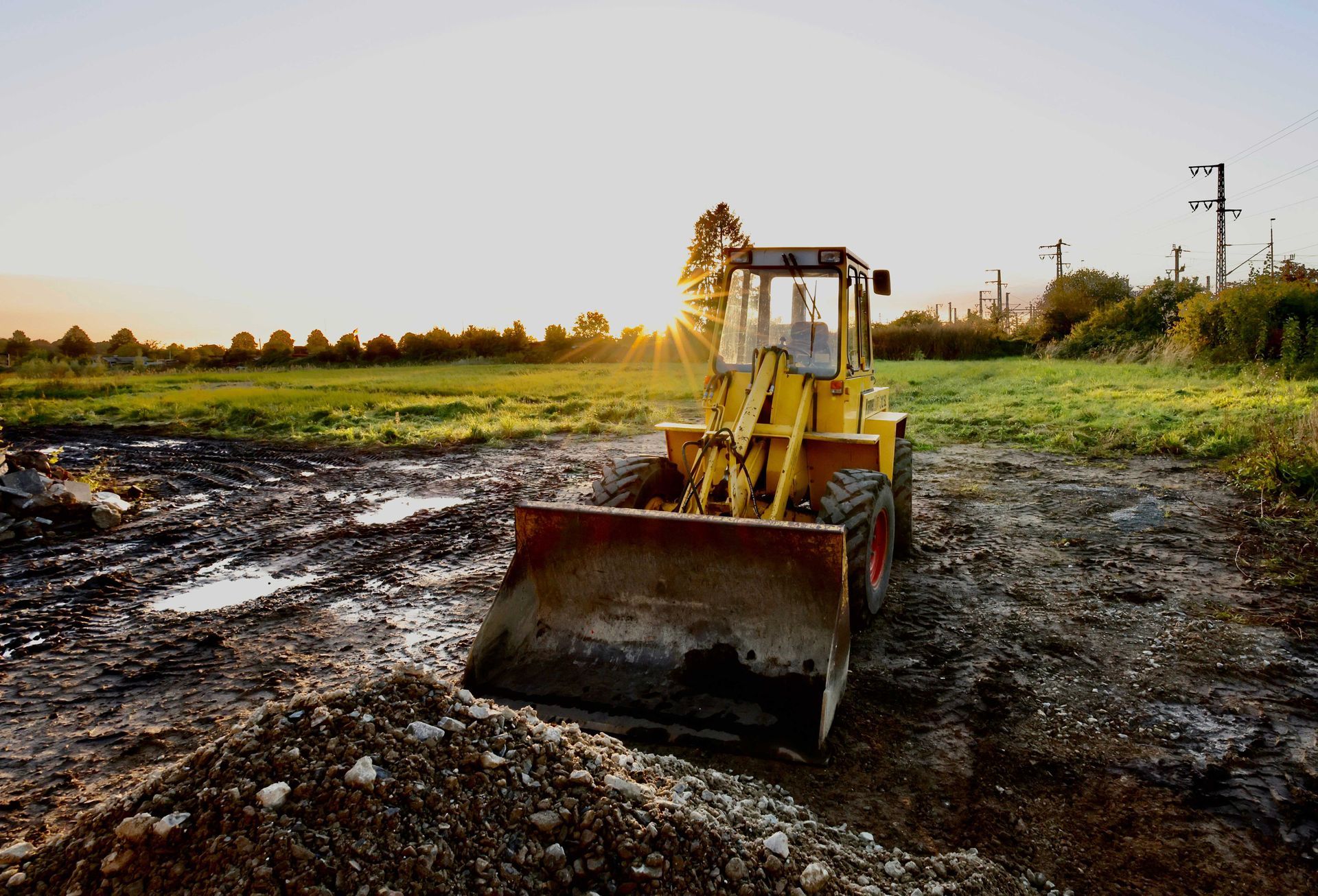 A yellow bulldozer is driving down a dirt road in a field.