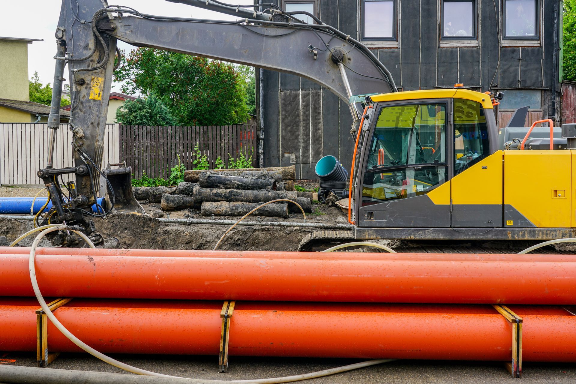 A yellow excavator is working on a construction site next to a pile of pipes.