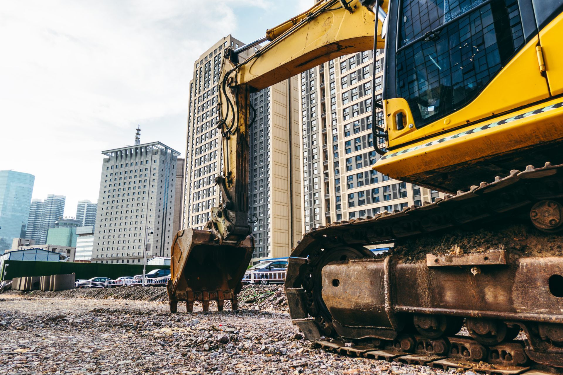 A yellow excavator is working on a construction site in front of a city.
