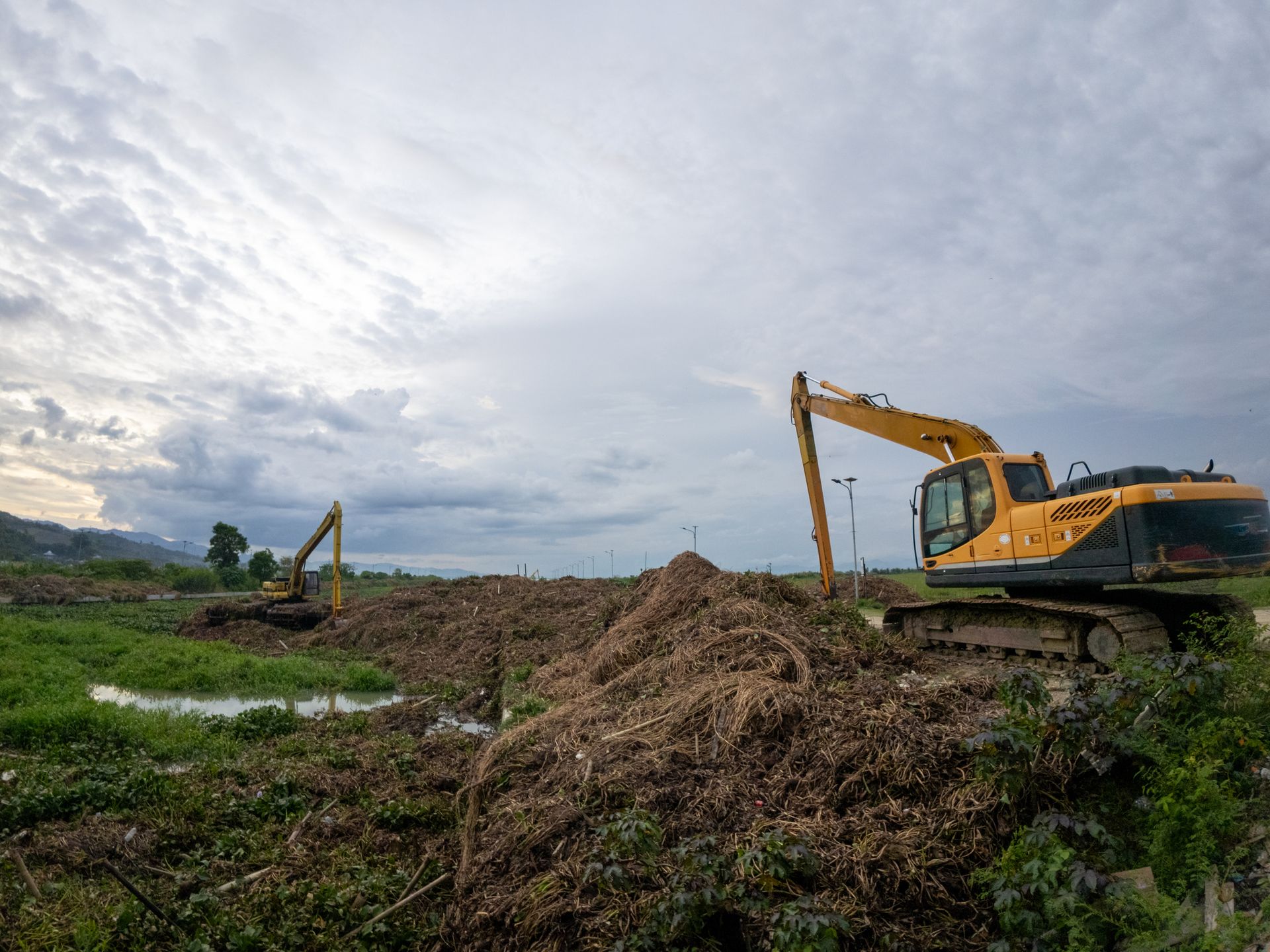 A yellow excavator is digging a pile of dirt in a field.
