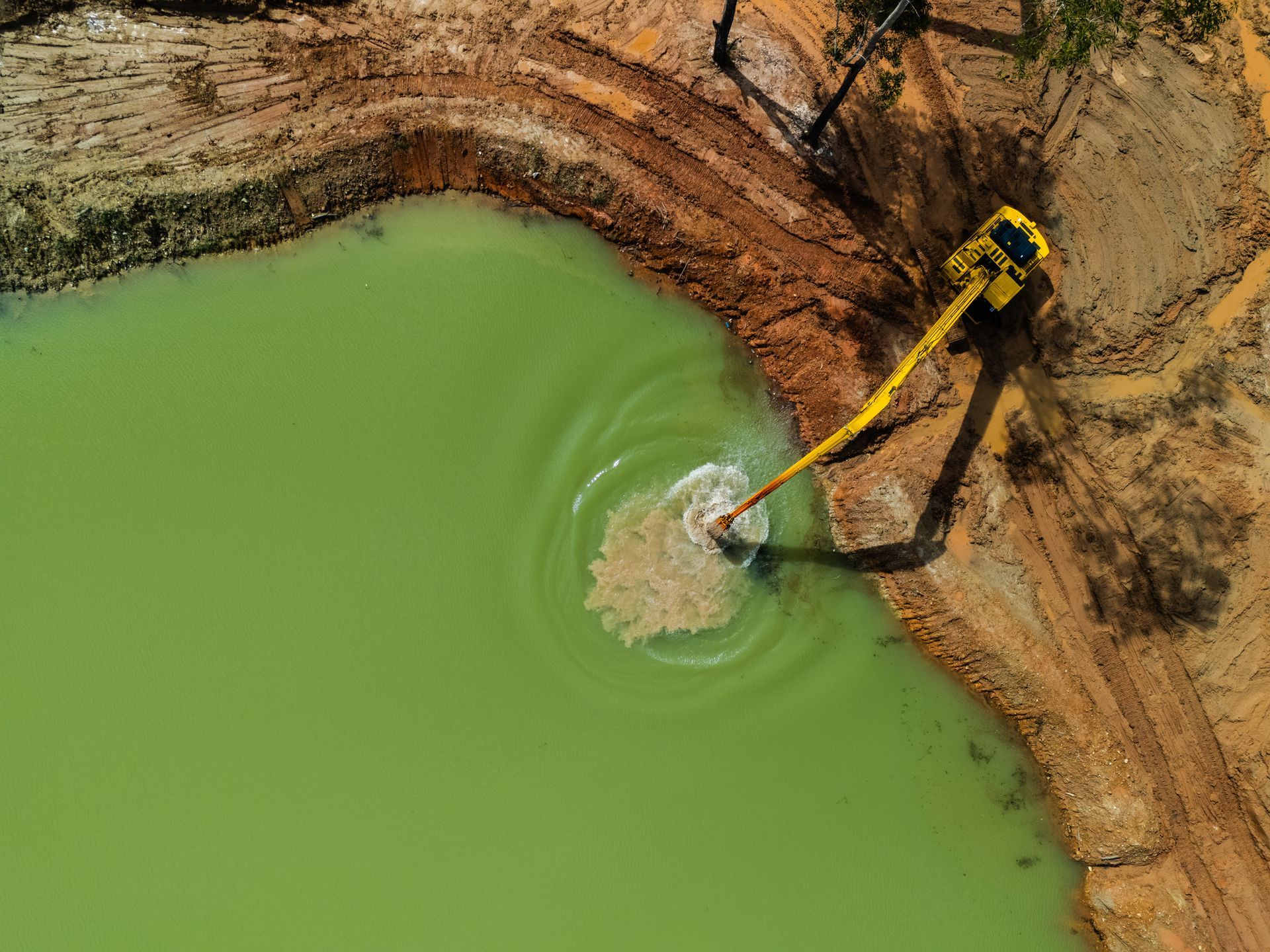 An aerial view of a yellow excavator digging a pond.