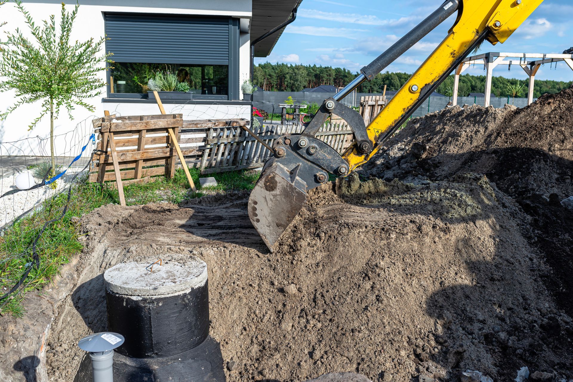 A yellow excavator is digging a hole in the ground in front of a house.