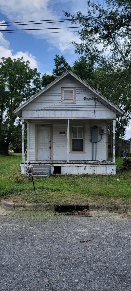 A Small White House With a Porch in the Middle of a Grassy Field