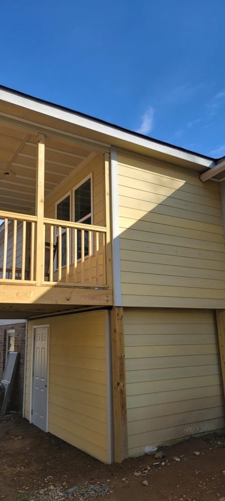 A Yellow House With a Balcony and a Garage Underneath It