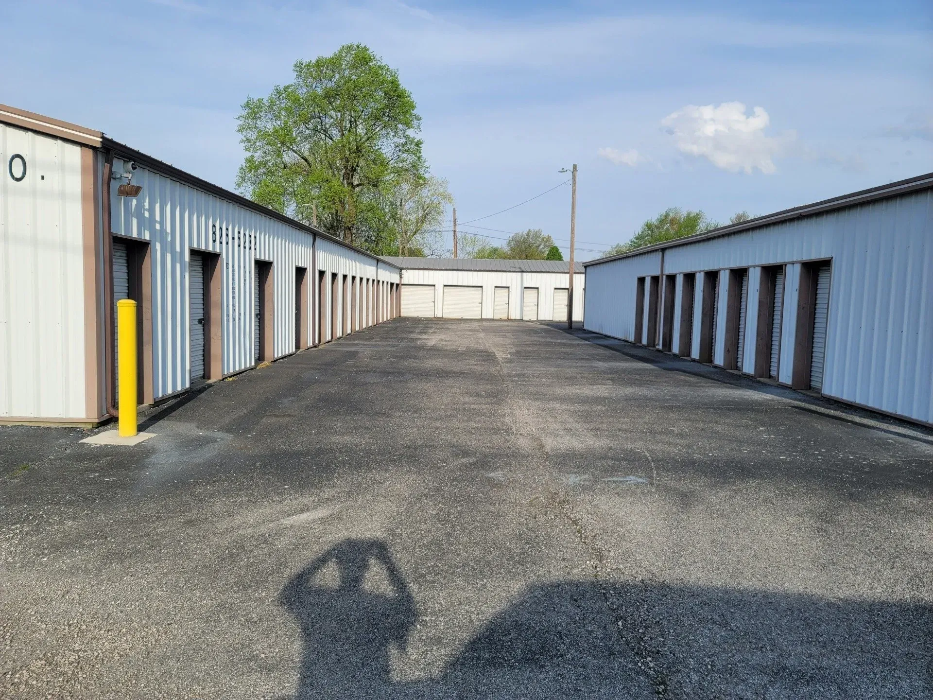 Storage units in a gravel lot, with a blue sky and a person's shadow visible.