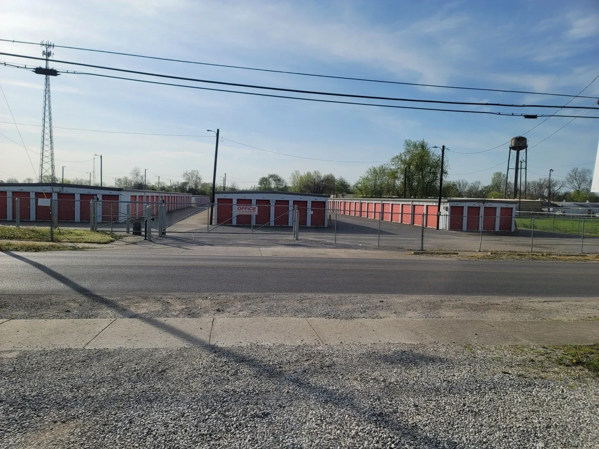 Storage units, red doors, gray road. Fenced area with a cell tower and water tower in the background.