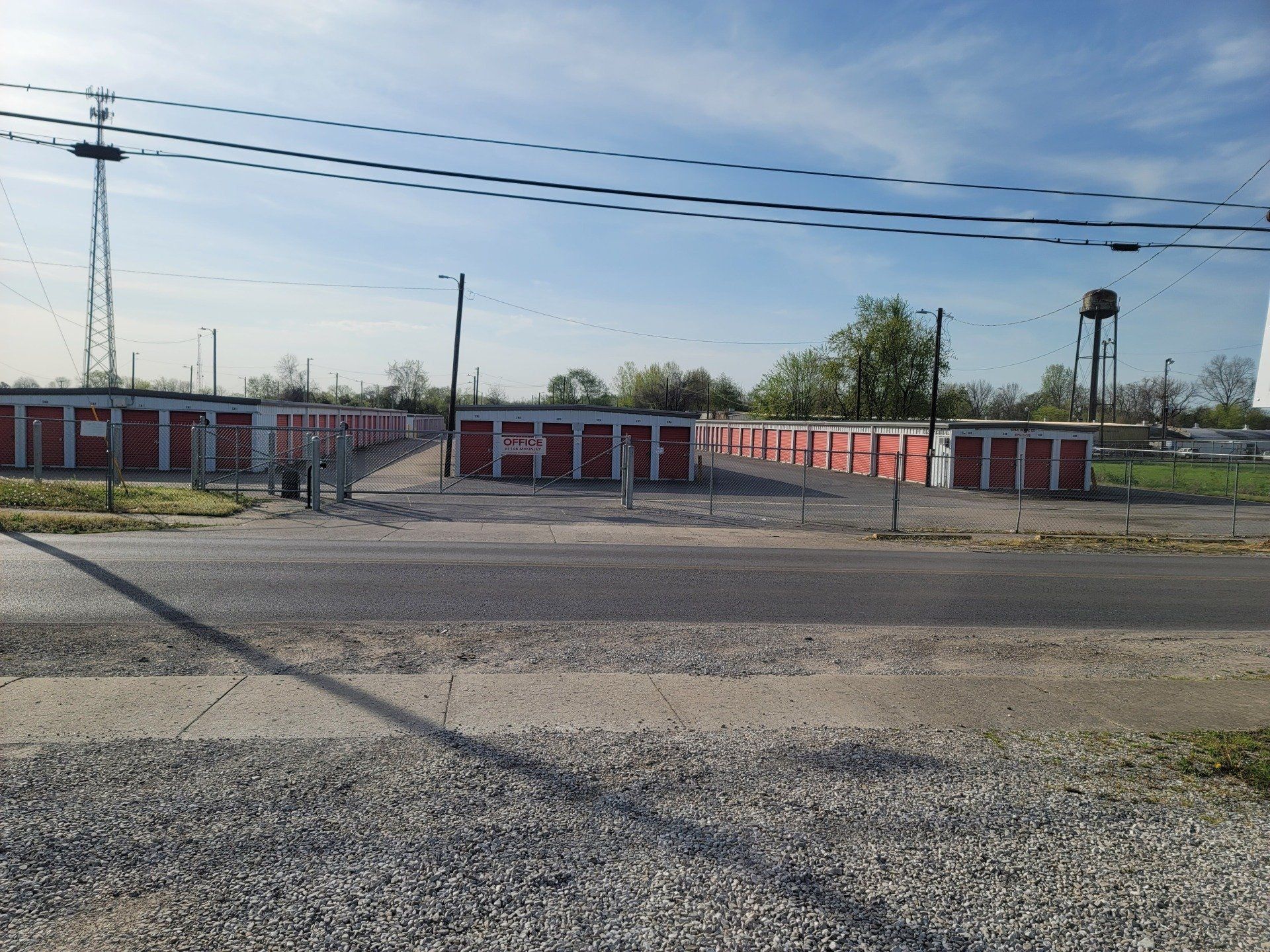 Storage units with red doors on a gravel lot, under a blue sky.