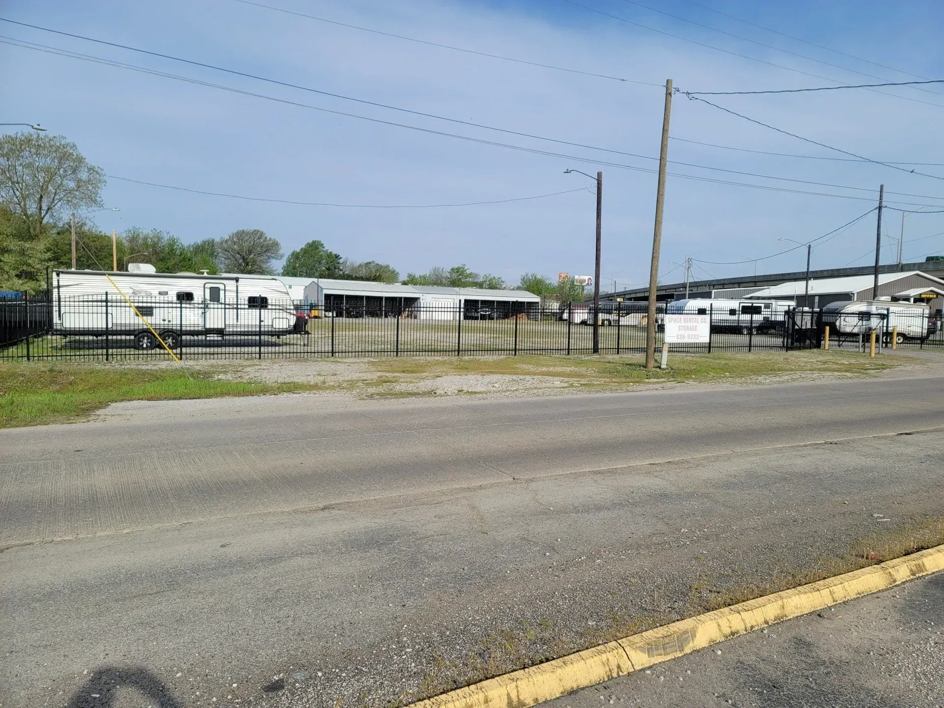 Campers and RVs parked behind a fence on an asphalt lot, utility poles overhead.