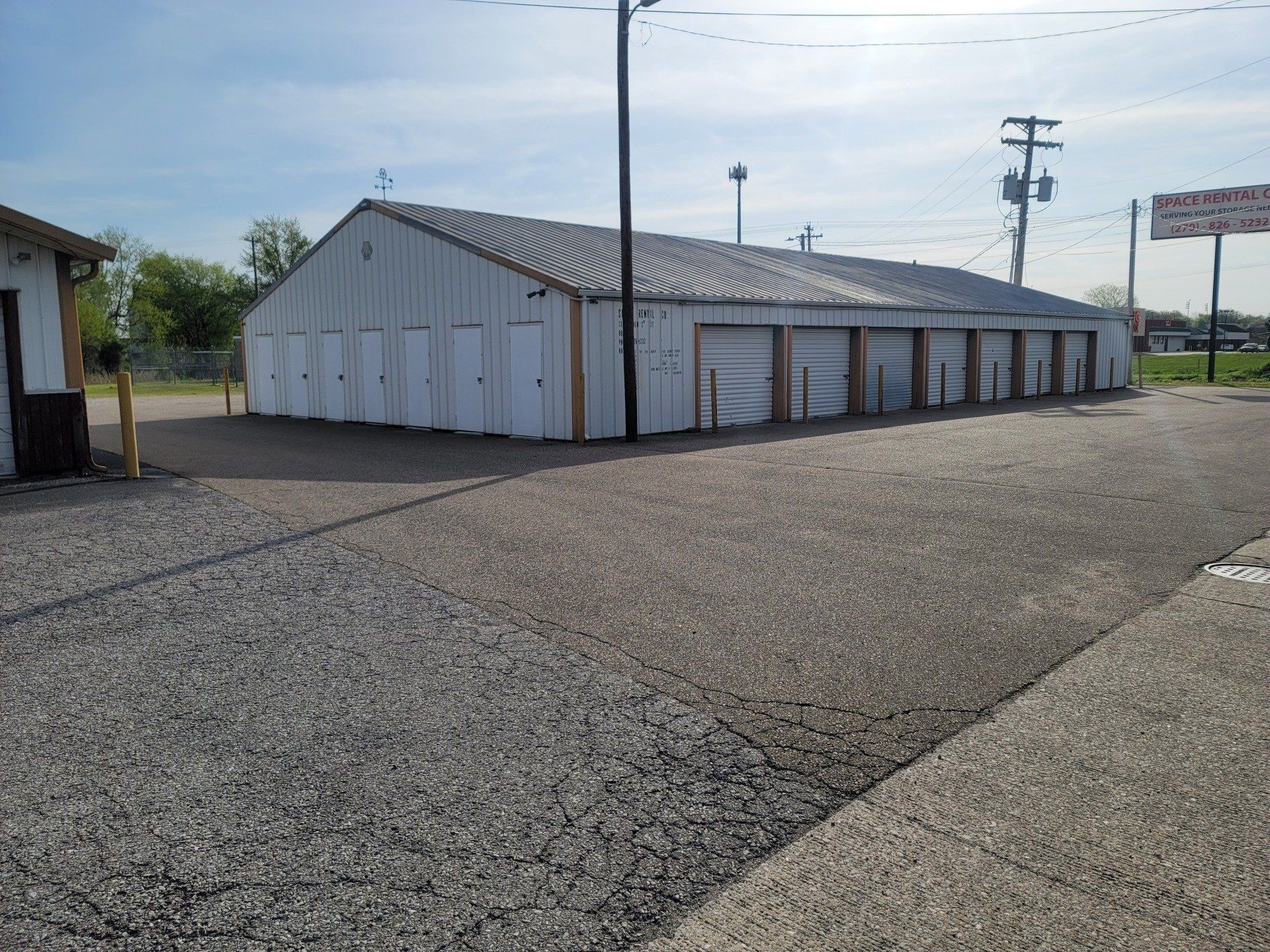 Storage units in a row, white doors, gravel lot, sunny day.