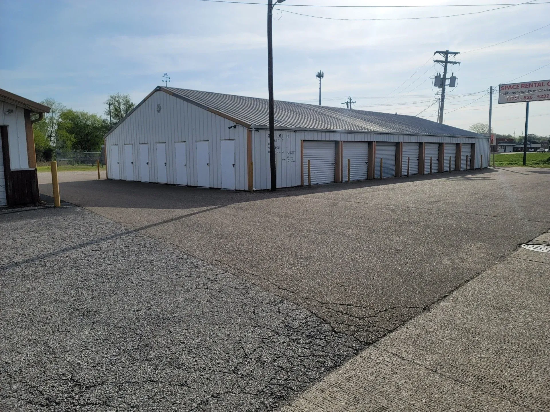Storage units, white doors, gray gravel lot, sunny day.