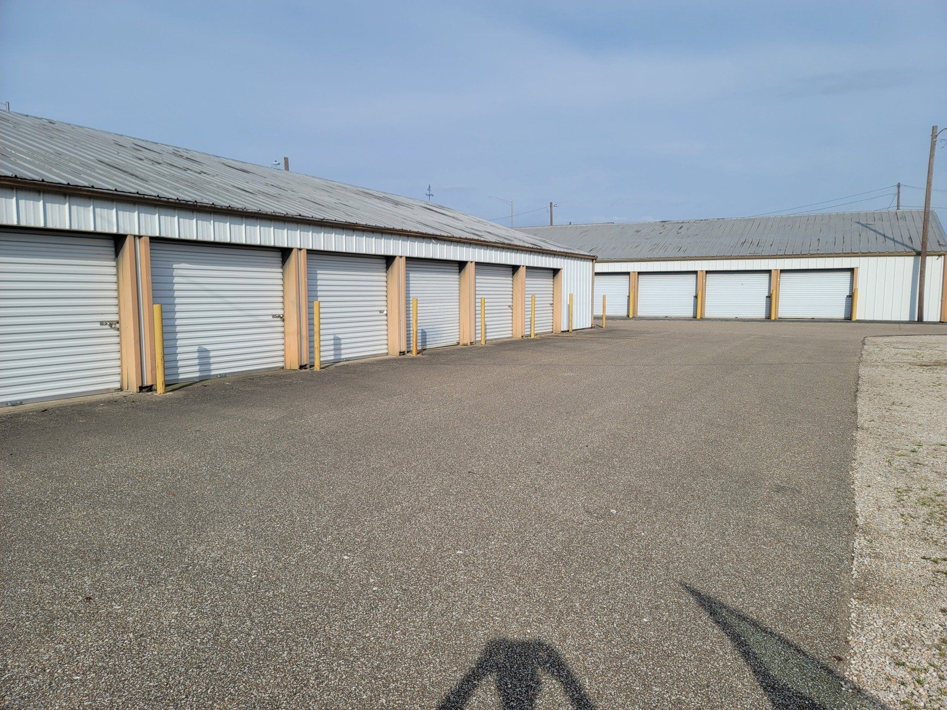Rows of storage units with gray doors and gravel ground.