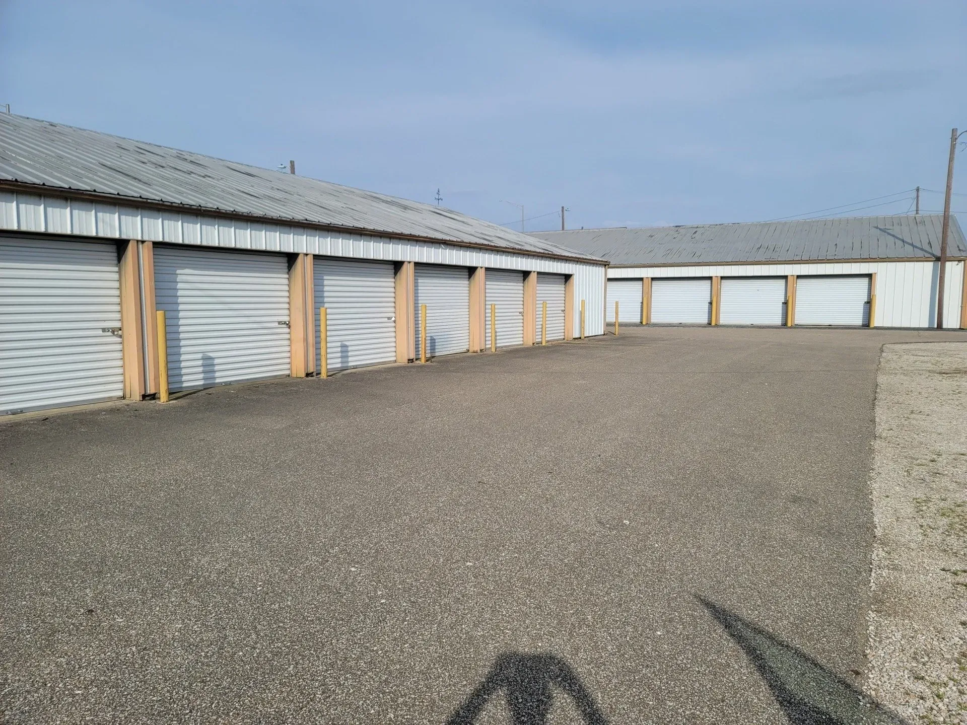 Storage units with gray metal doors and roofs, on a gravel lot under a clear sky.