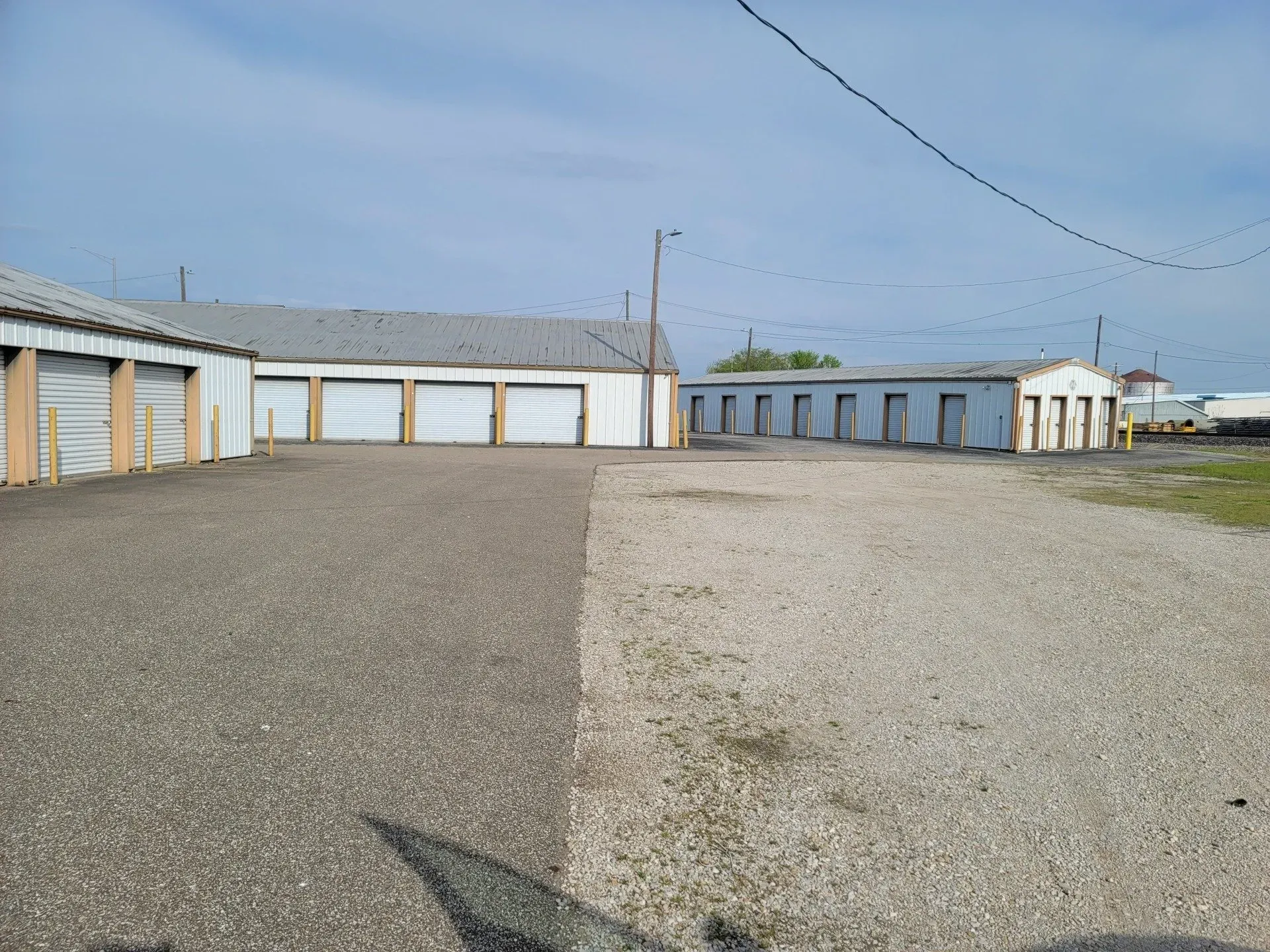 Storage units with gray doors and roofs, gravel drive, and blue sky.