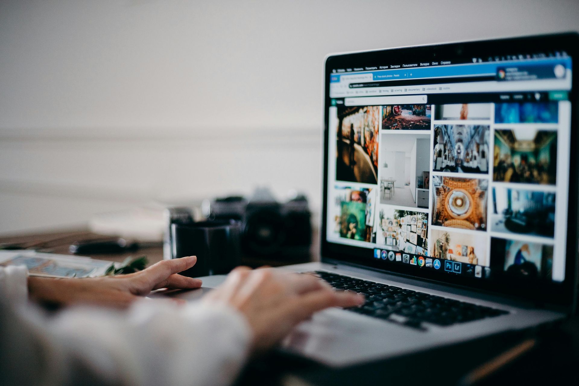 A person is typing on a laptop computer with a camera in the background.