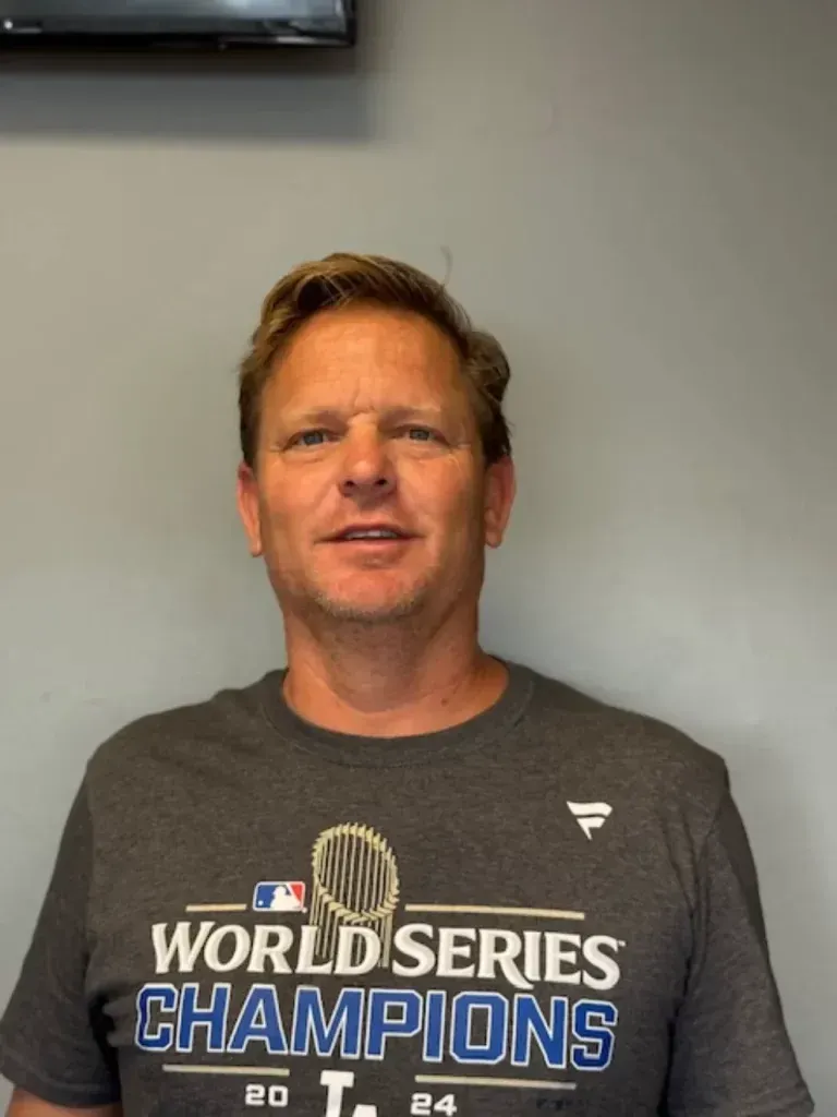 Man in gray World Series Champions T-shirt standing against a plain wall, smiling at the camera.