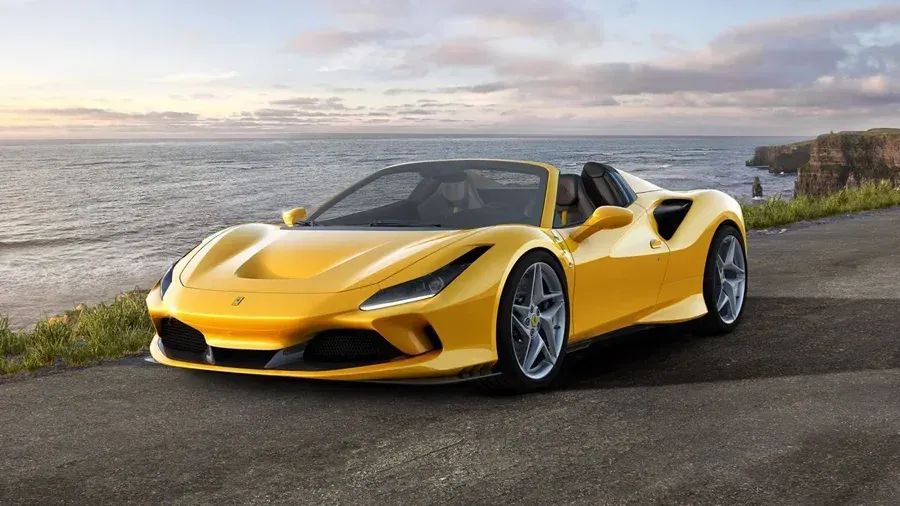Yellow sports car parked on a coastal road with ocean and sunset in the background