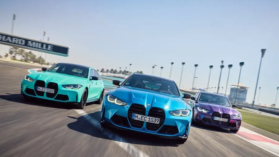 Three BMW race cars speed side by side on a track, blue centered, turquoise left, purple right.