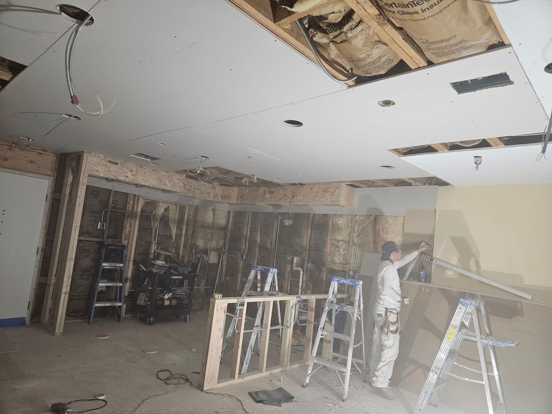 Construction workers renovating a room with exposed ceiling, ladders, and drywall demolition debris