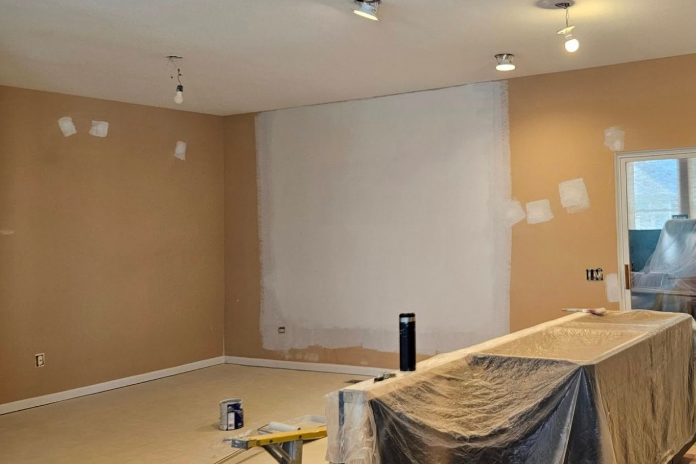 Partially painted room with tan walls, a gray accent wall, and a covered table in the foreground