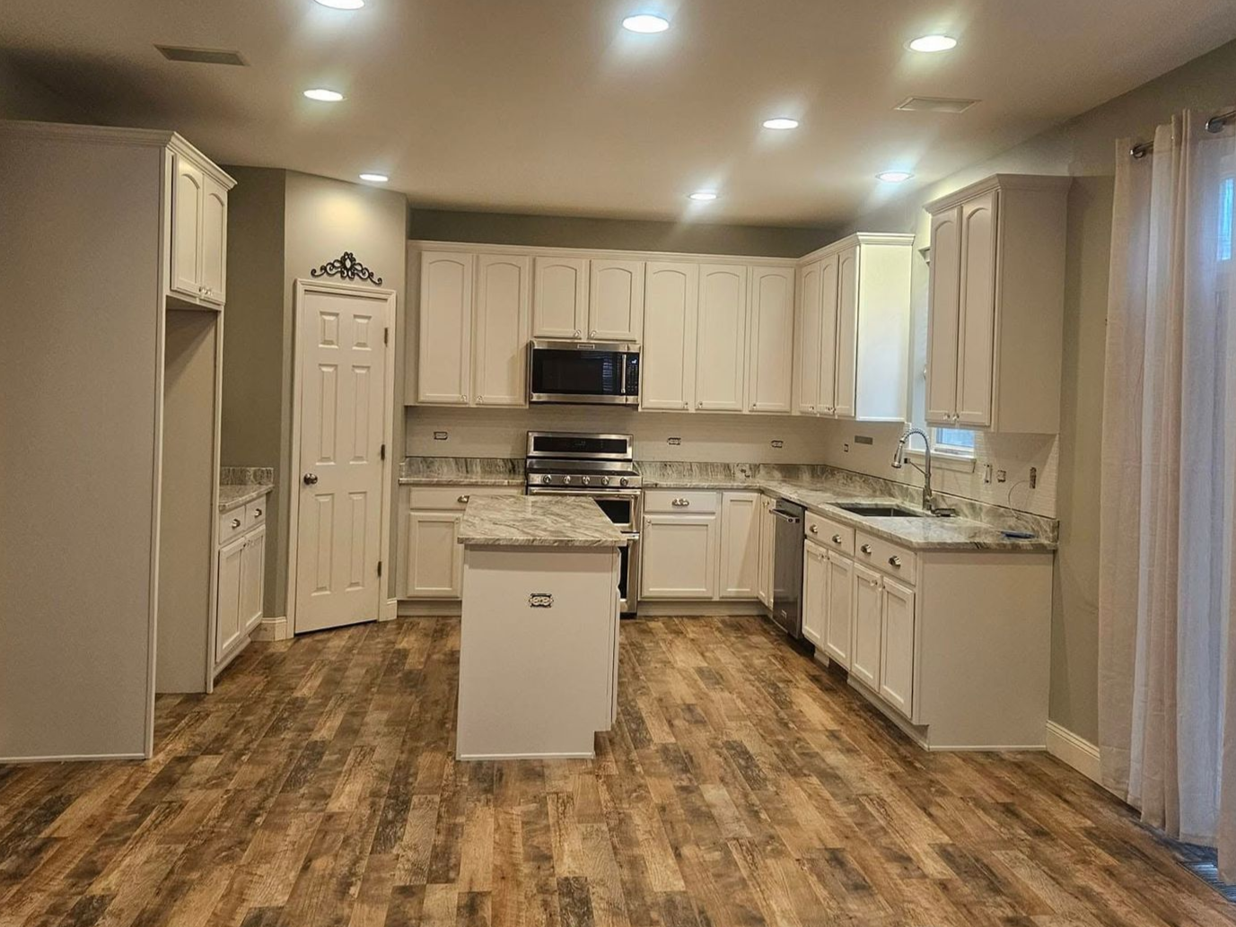 Modern kitchen with white cabinets, granite counters, stainless appliances, and wood-look flooring