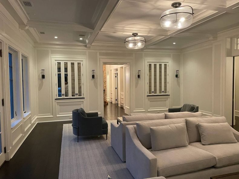 Elegant living room with white sofas, dark chair, and ceiling lights in a bright, paneled interior
