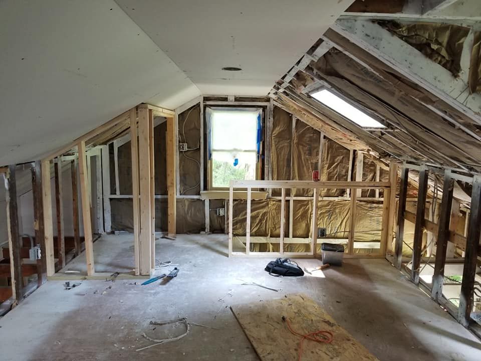 Unfinished attic renovation with exposed wooden framing, sloped roof, and a bright window at the far end