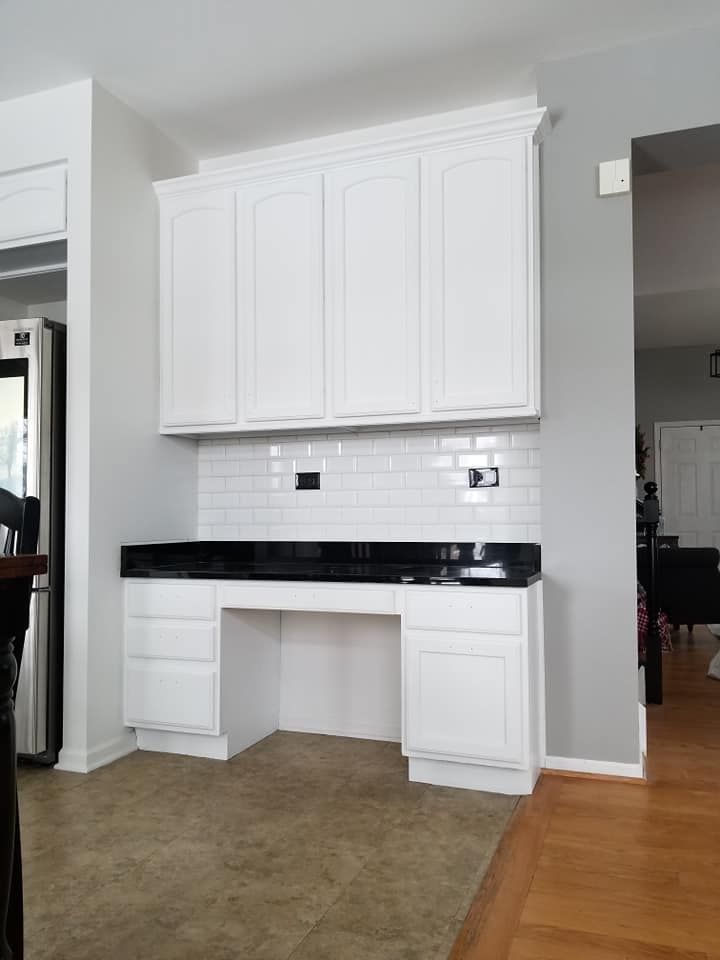 White built-in cabinets and black countertop against a tiled wall in a bright room.