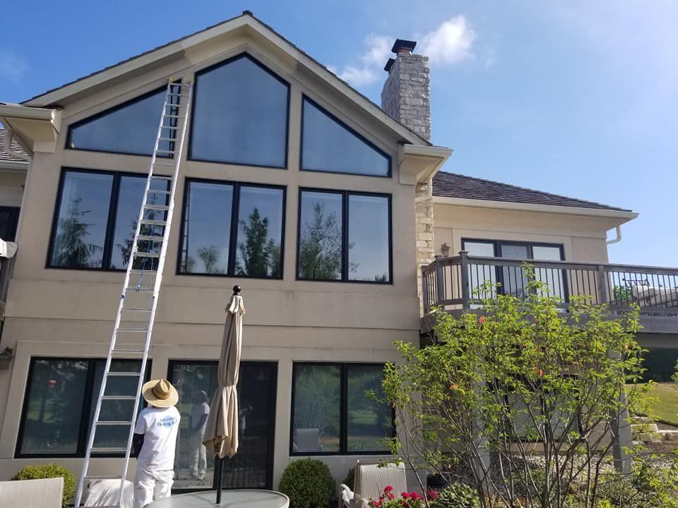 Person on a ladder painting the exterior of a two-story house with large windows and a deck.