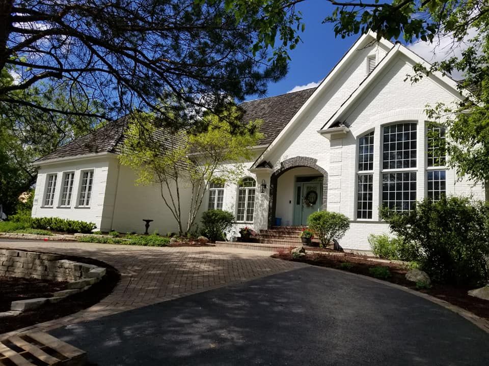 White suburban house with a curved driveway, front porch, and large arched window under trees
