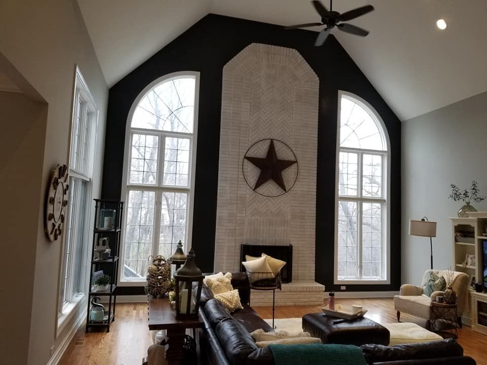 Spacious living room with tall arched windows, vaulted ceiling, black fireplace wall, and rustic decor