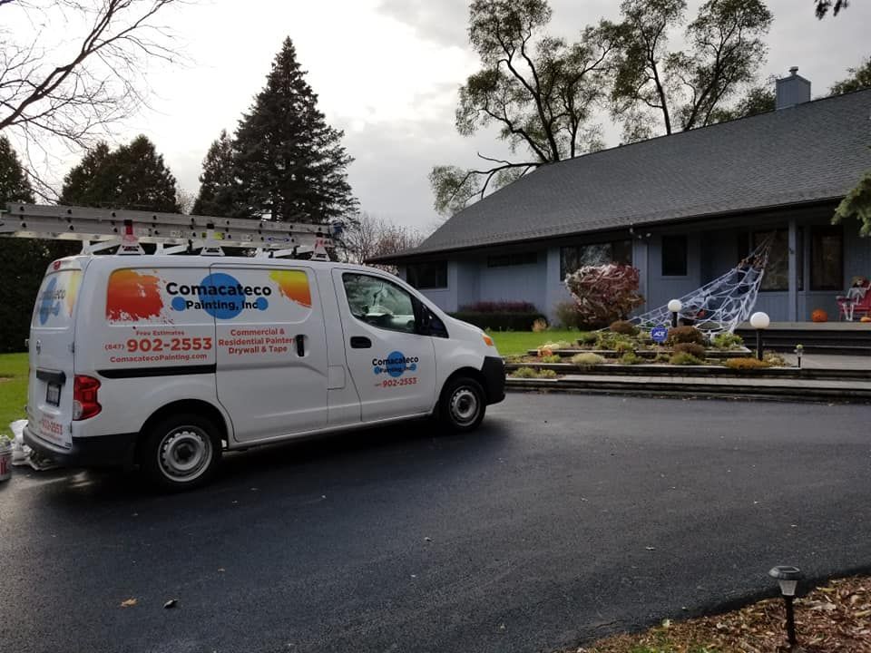 White service van parked on a wet street in front of a house with a garden, cloudy day