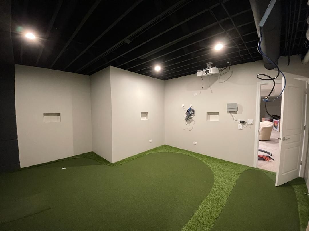 Empty indoor room with green turf flooring, white walls, and exposed black ceiling beams