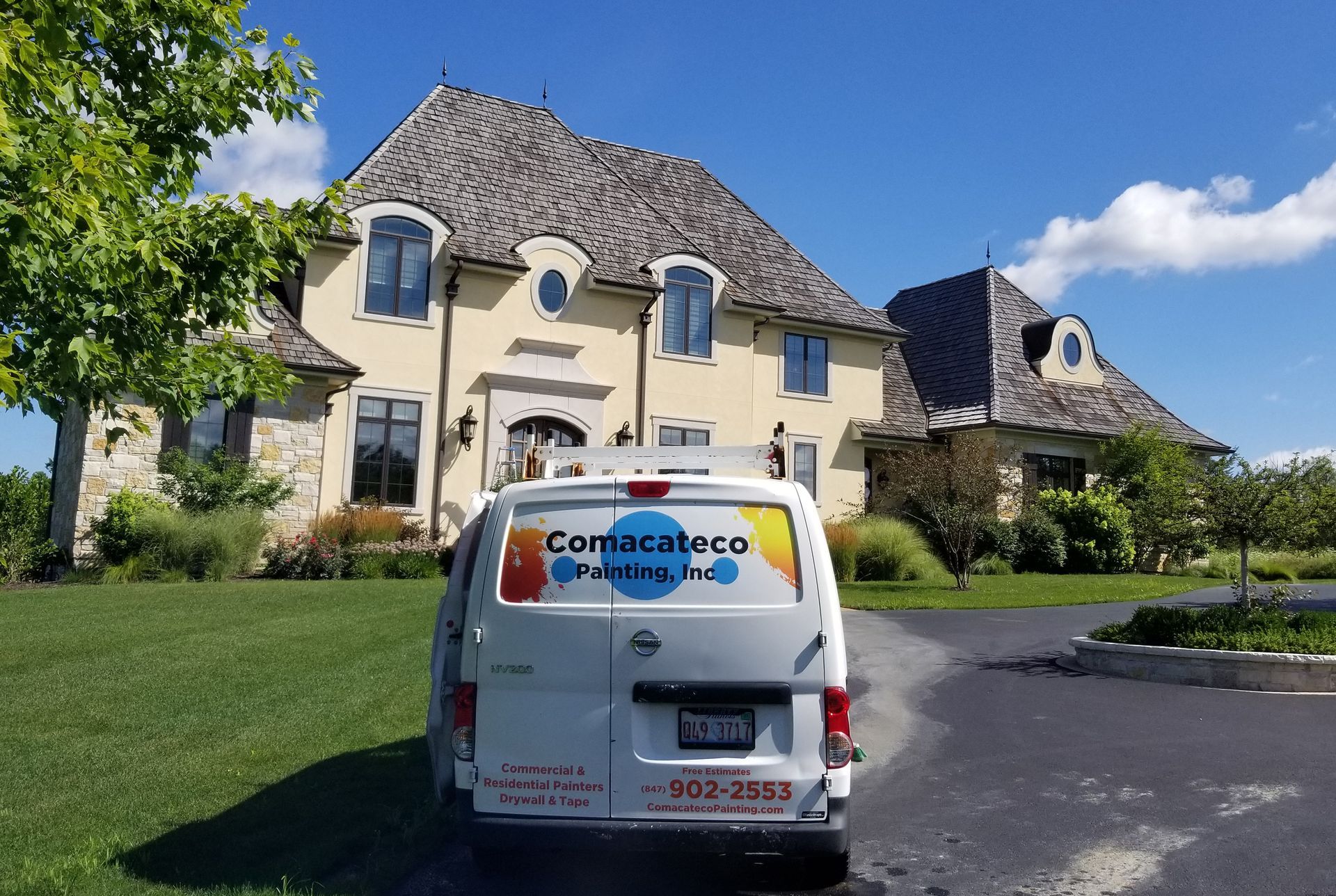 White service van parked before a large beige house with a blue sky and green lawn.
