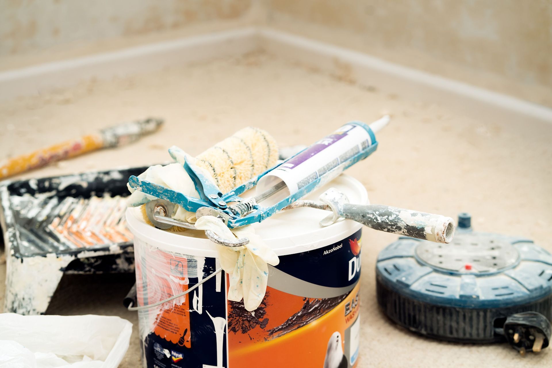 Paintbrushes and paint cans with a tape measure and small tool on a dusty work surface