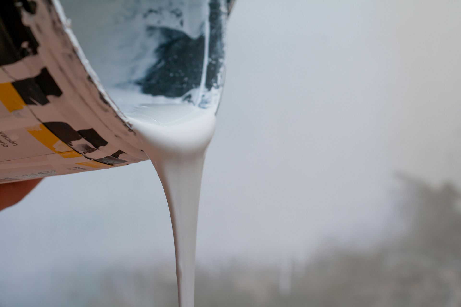 White liquid pouring from a container against a blurred gray background