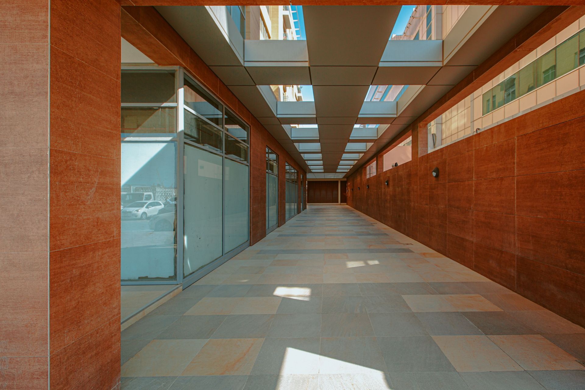 Empty modern corridor with glass walls, brick walls, and skylights casting light on the tiled floor