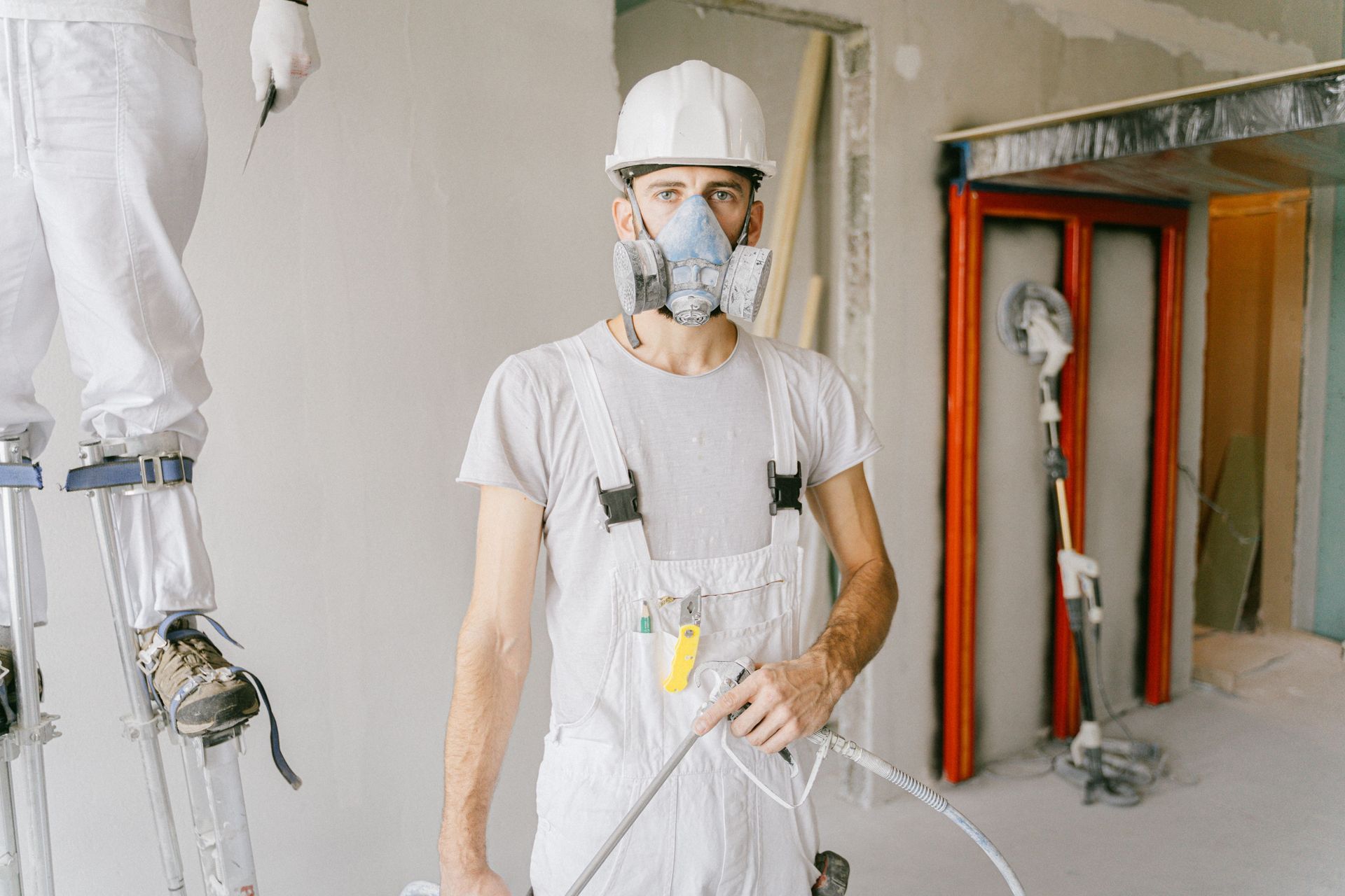 Worker in white protective gear and respirator in a construction area, holding a hose.