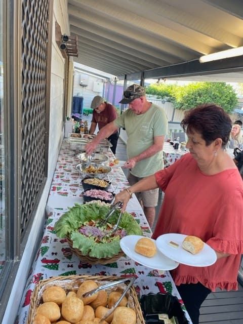 A Group Of People Are Standing Around A Table Eating Food — Tru Blu Catering In Sawtell, NSW