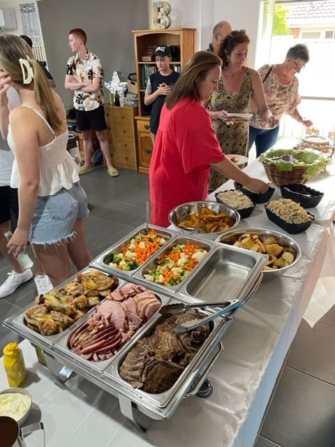 A Group Of People Are Standing Around A Buffet Table Filled With Food — Tru Blu Catering In Coffs Harbour, NSW